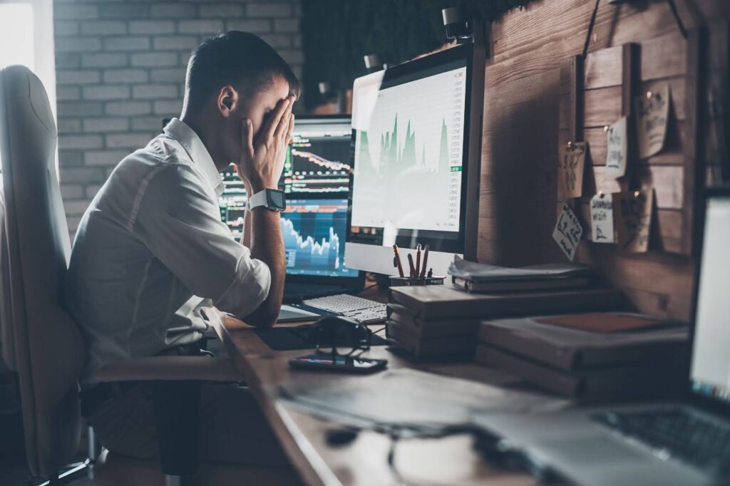 Man sitting in front of his work computer with his screens on and his head in his hands